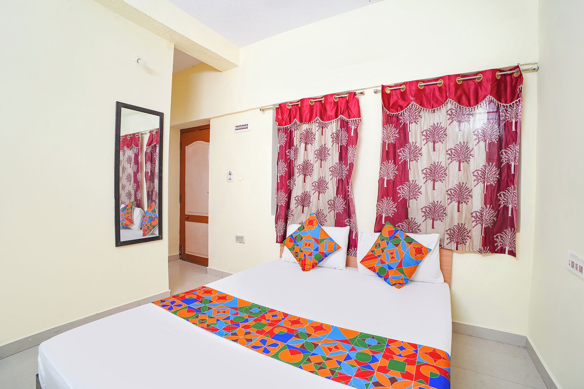A bedroom with a bed, curtains, a mirror, and a door.