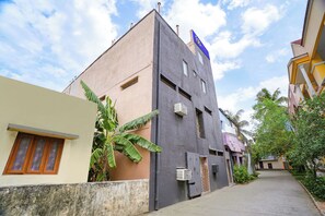 A narrow street with buildings, including a two-story structure with a blue sign, a small window, and an air conditioning unit.