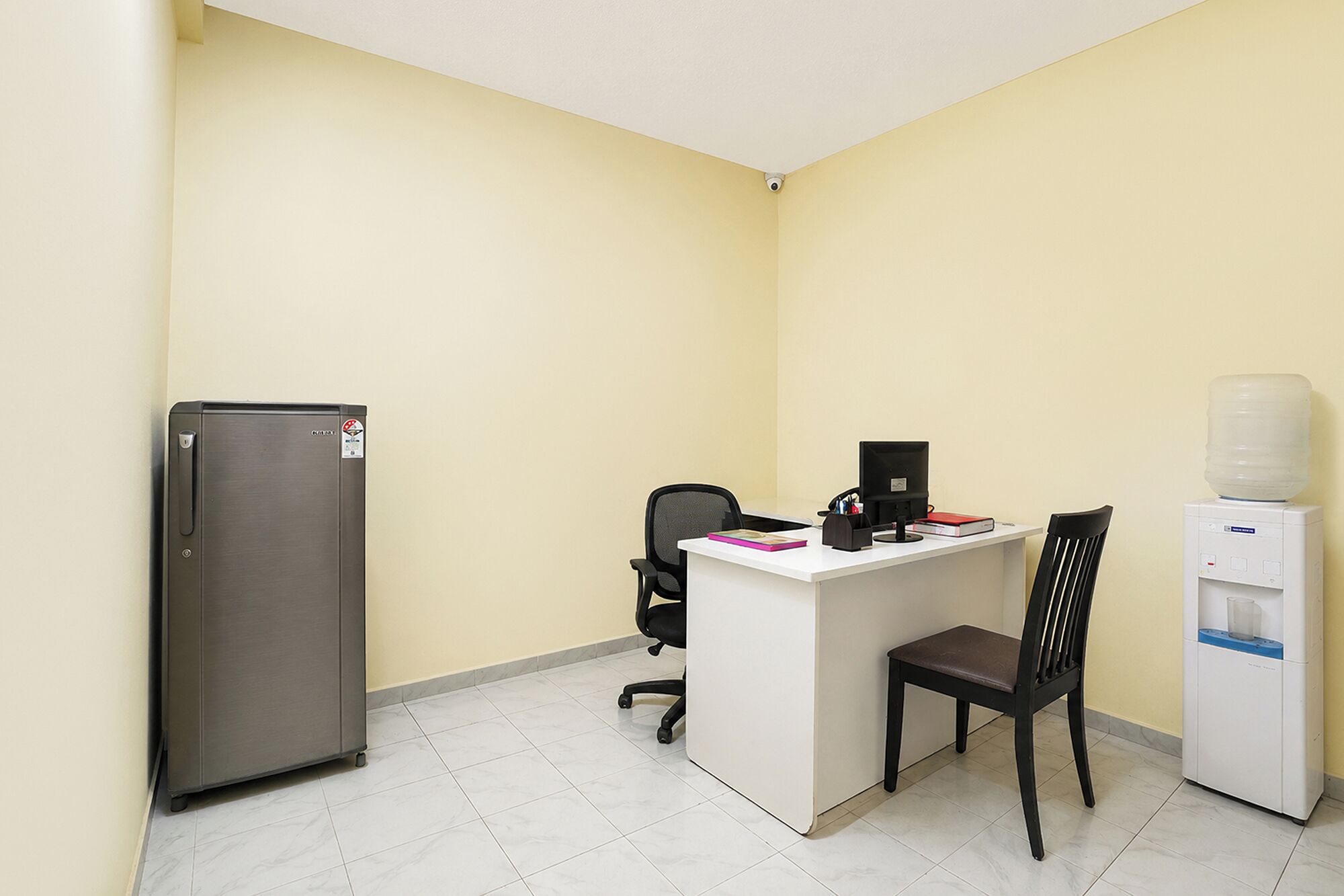 A small office with a desk, chair, computer, refrigerator, and water dispenser.