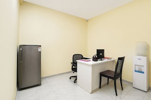 A small office with a desk, chair, computer, refrigerator, and water dispenser.