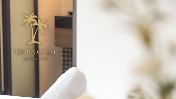 A neatly made bed with a towel and a decorative item, a window with a reflection, and a logo for Terra Calm Residence. - Terra Calm Private Pool Villa (Da Nang)