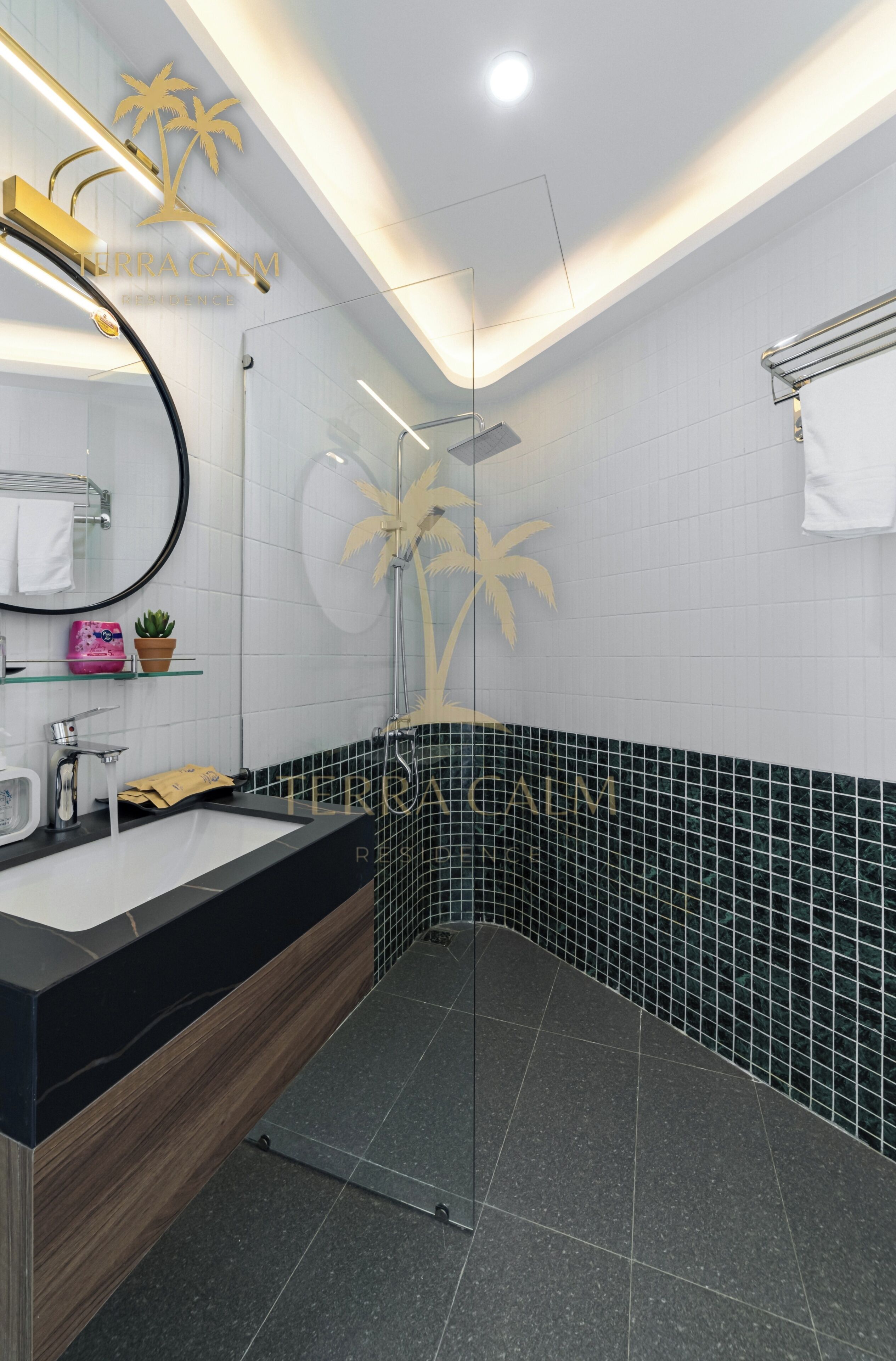 Un baño moderno con encimera negra, cabina de ducha de cristal y pared de azulejos blancos con diseños de palmeras.
