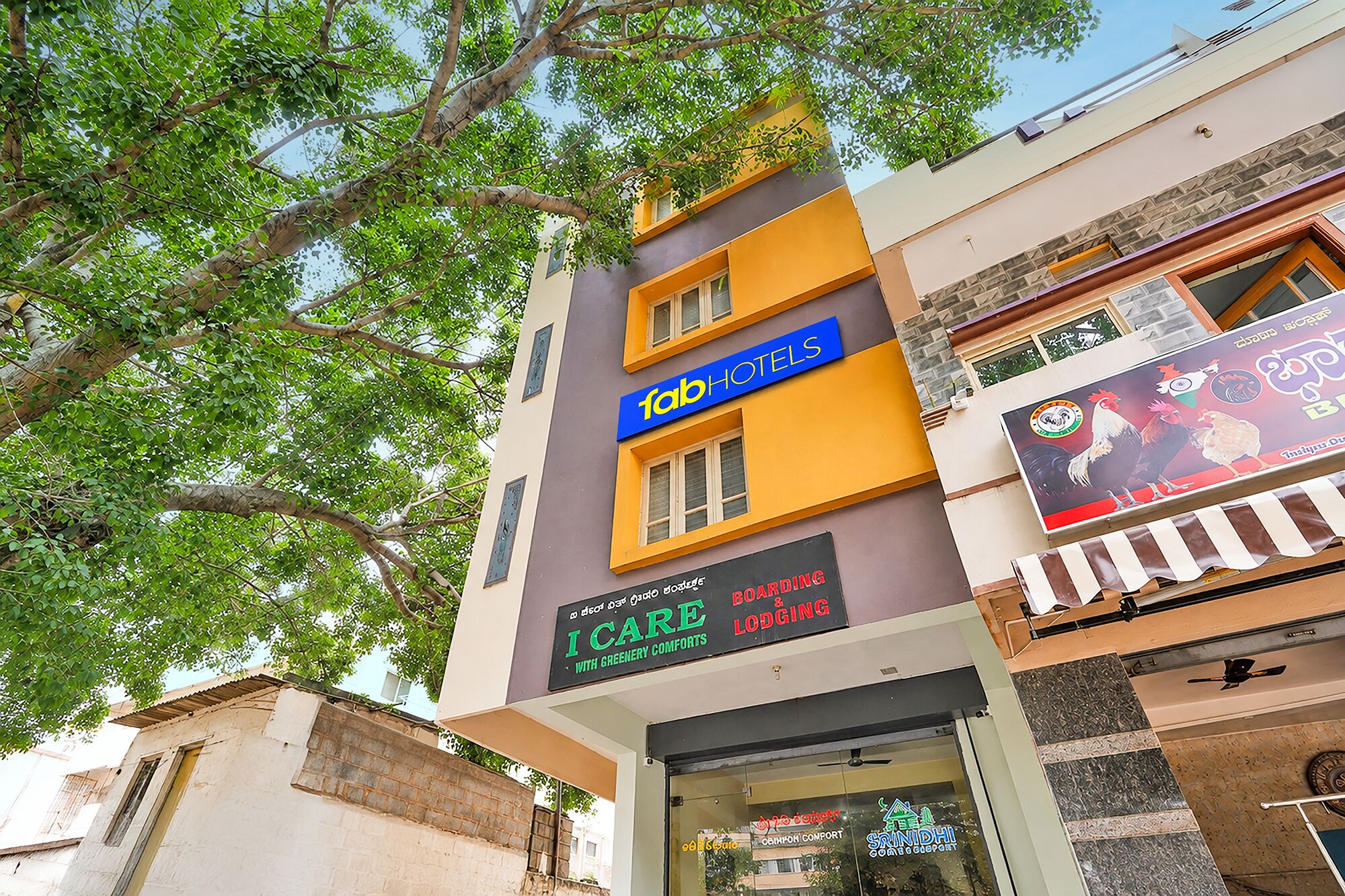 A multi-story building with a sign for 'fabHOTELS' and another sign for 'ICARE WITH GREENERY COMFORTS'.