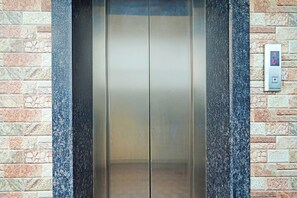 An elevator with a control panel on the wall, surrounded by a stone wall.