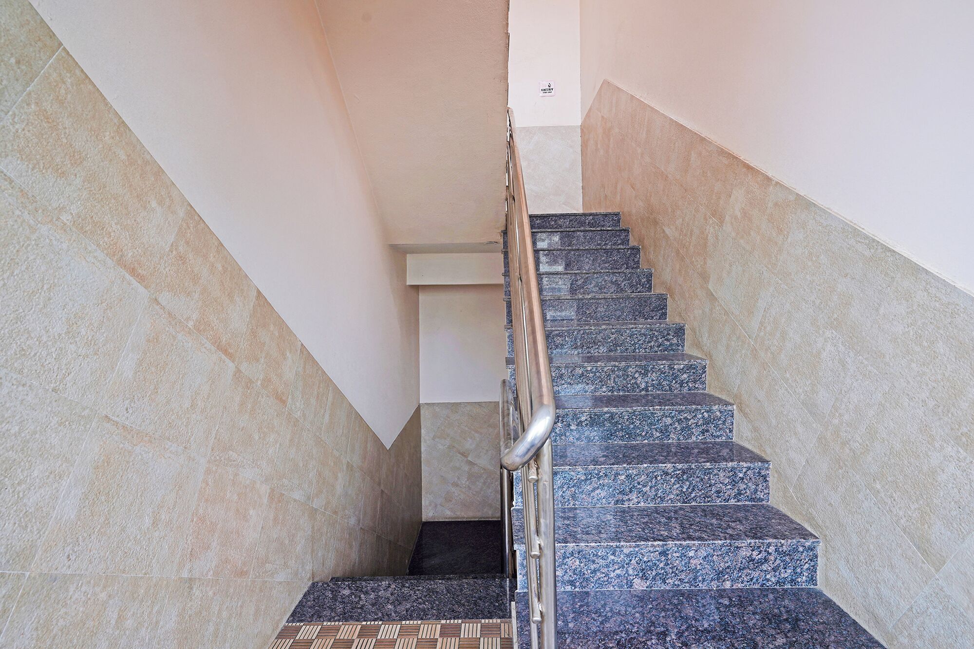 Una escalera con barandilla de metal, paredes color beige y piso de baldosas.