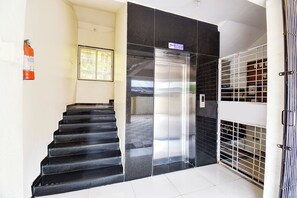 Eine Treppe führt zu einem Aufzug, an der Wand hängt ein Feuerlöscher und ein Sicherheitstor ist vorhanden.