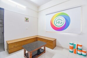 A room with a wooden bench, a whiteboard with a colorful logo, and a small potted plant. - FabHotel Himalay Guest House Saanvi Residency (Pune)