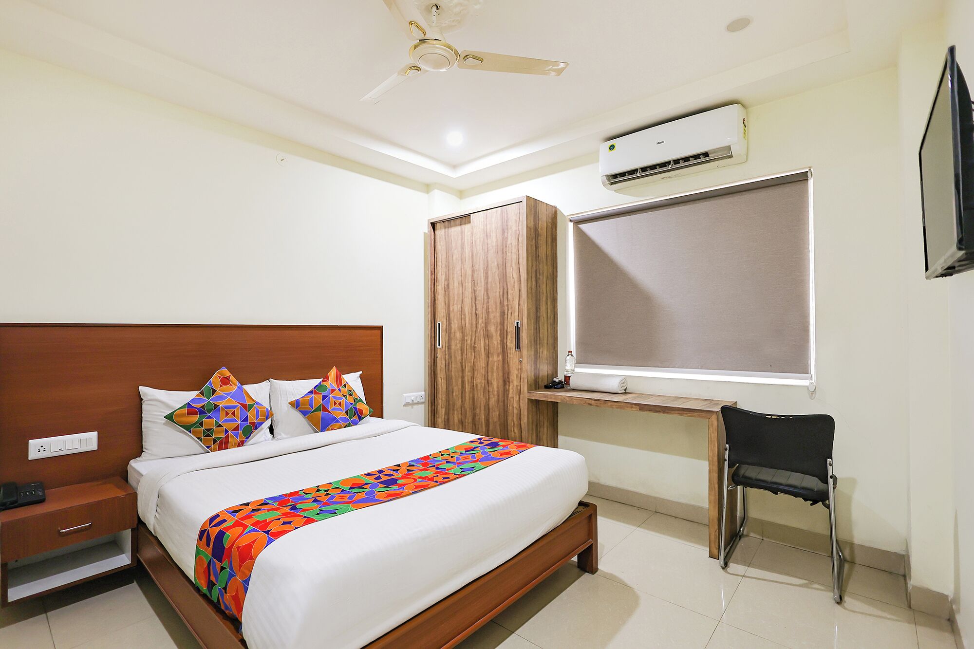 Habitación de hotel con cama, escritorio, silla, aire acondicionado y ventilador de techo.