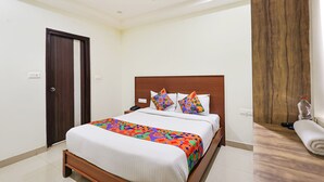 A bedroom with a bed, a wooden headboard, a ceiling fan, and a door. - Fabhotel Ram Nivas (Atchutapuram)