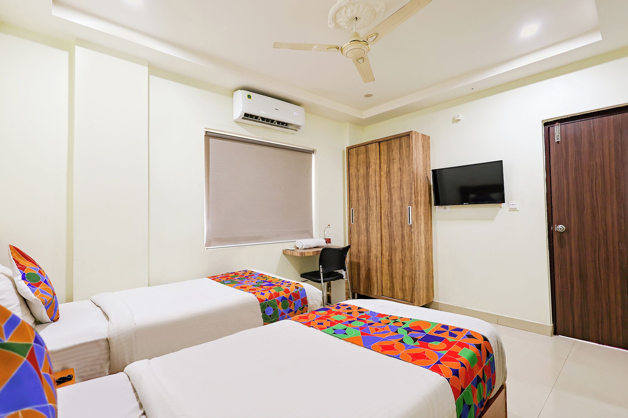 Une chambre d’hôtel avec deux lits, un ventilateur de plafond, un appareil de climatisation, une télévision et une armoire en bois.