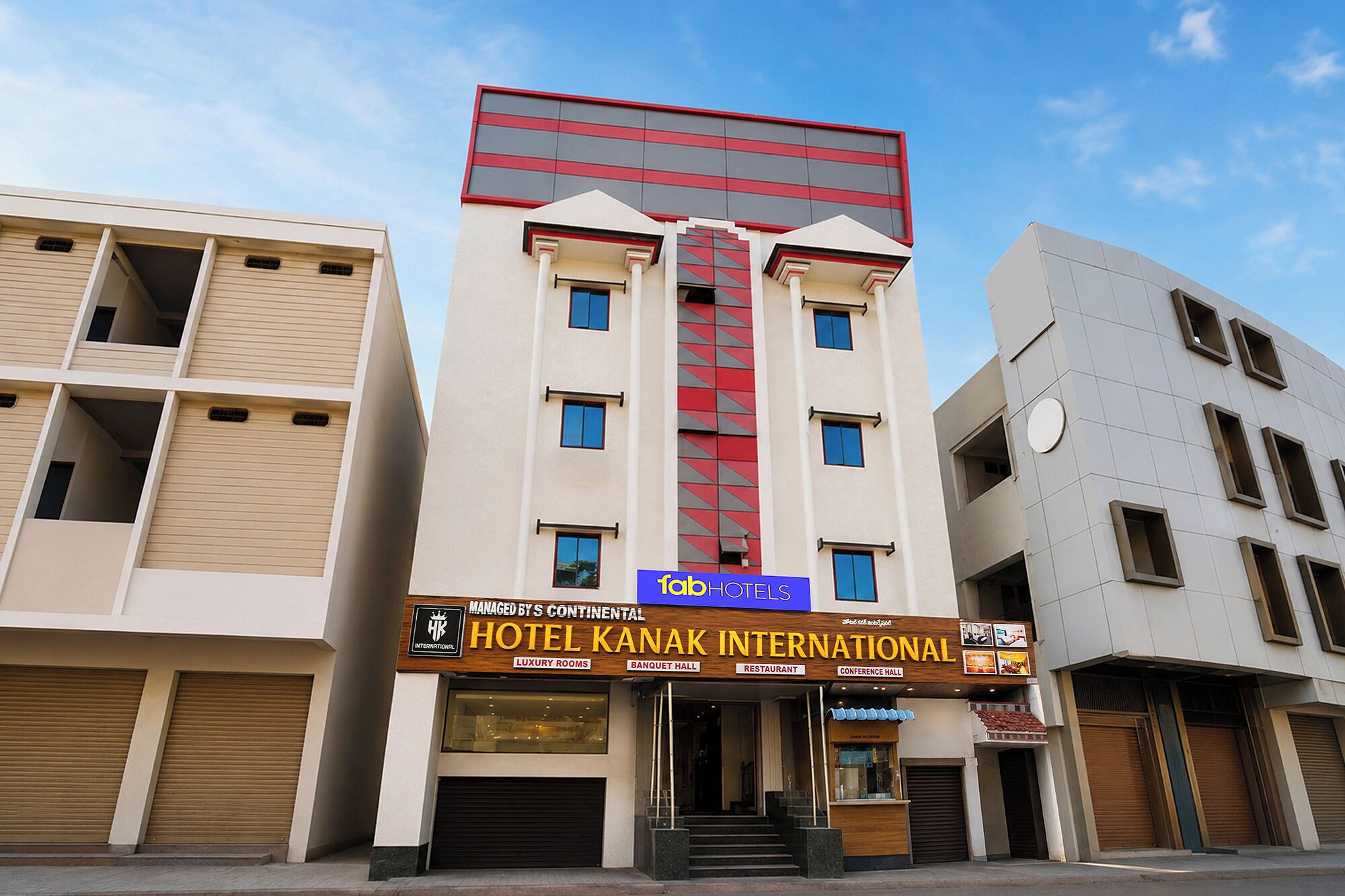 A hotel building with a sign for 'Hotel Kanak International' and amenities including luxury rooms, banquet hall, restaurant, and conference hall.