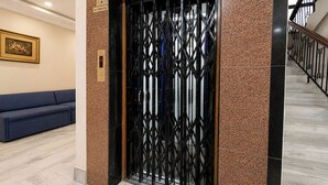 Um elevador com portão de metal preto, sofá azul e uma placa fixada na parede.