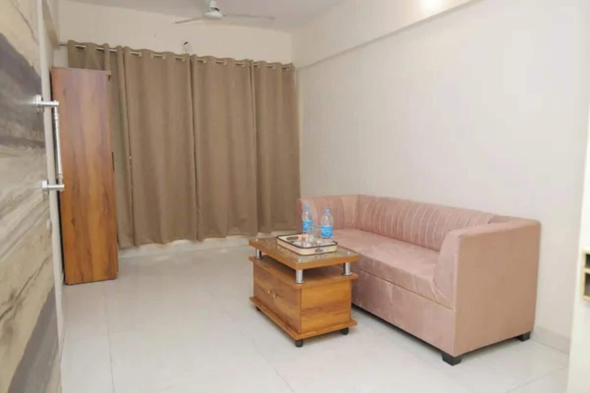 Una habitación con un sofá, una mesita de madera con botellas, una puerta y una cortina.