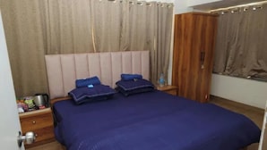 A bedroom with a bed, curtains, a wardrobe, and a nightstand with a kettle. - Fabhotel Aqua Pearl Inn (Panvel)