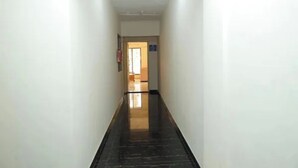 A corridor with white walls and a shiny black floor, leading to a door at the end. - Fabhotel Aqua Pearl Inn (Panvel)