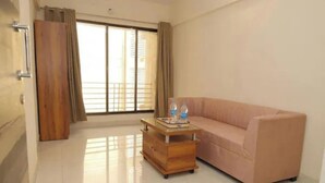 A room with a sofa, a wooden side table with a tray, and a window with curtains. - Fabhotel Aqua Pearl Inn (Panvel)