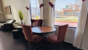 A room with a round table, two chairs, a sofa, a coffee table, a plant, and a window with curtains.