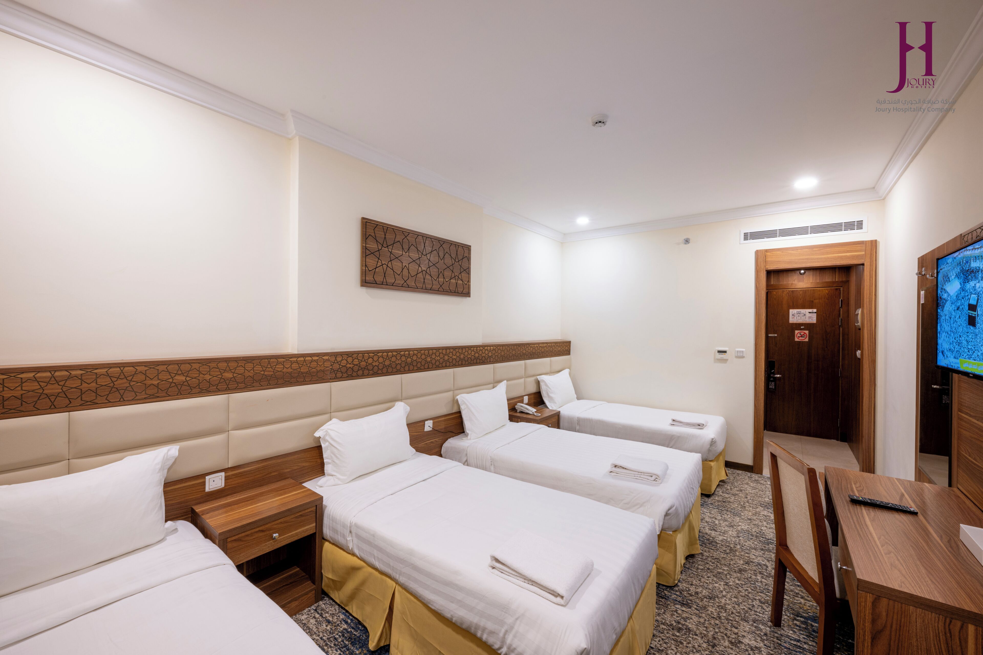Habitación de hotel con cuatro camas, cabecera de madera, televisión, escritorio y una puerta.