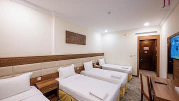 Habitación de hotel con cuatro camas, cabecera de madera, televisión, escritorio y una puerta.