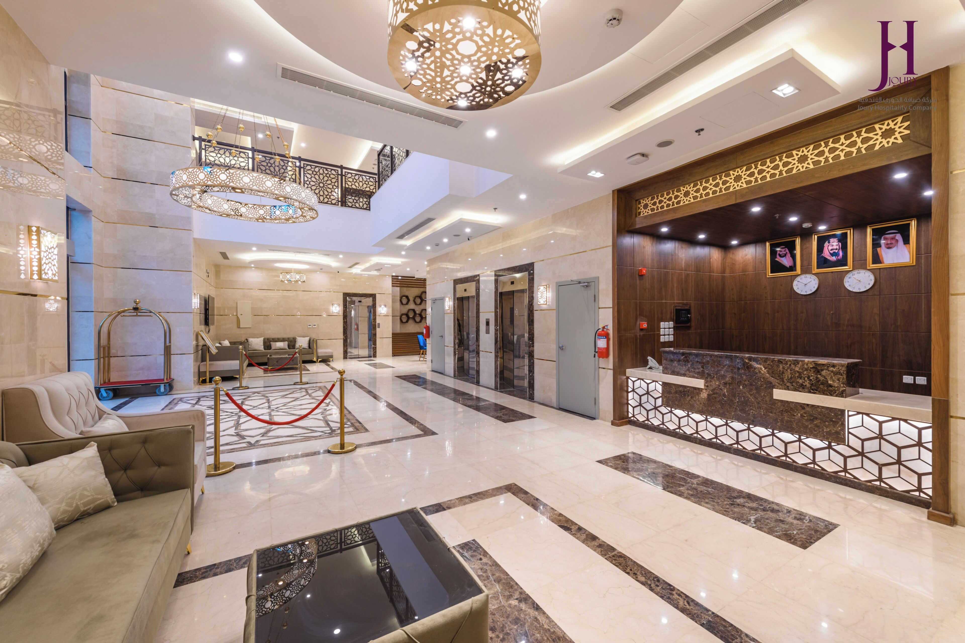 Un vestíbulo de hotel con una recepción, una escalera, un sofá y un candelabro.