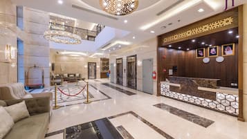 Un vestíbulo de hotel con una recepción, una escalera, un sofá y un candelabro.