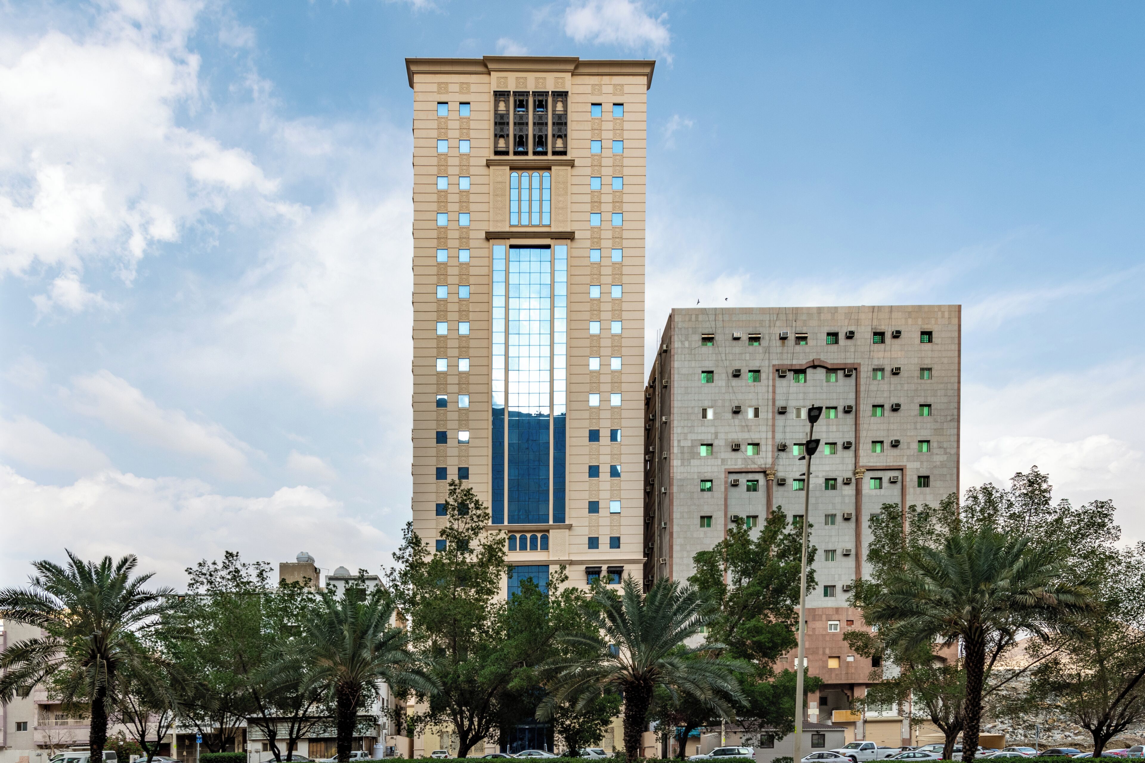 Um edifício alto com design moderno, rodeado por palmeiras e outros edifícios.