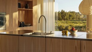 A modern kitchen with wooden cabinets, a stainless steel sink, and a view of a green landscape through large windows. - Architect Hideaway Between Heath & the North Sea (Brovst)