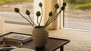 A modern interior with a large window, a textured rug, a wooden coffee table, and a vase with dried flowers. - Architect Hideaway Between Heath & the North Sea (Brovst)