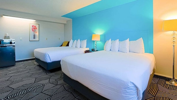 A hotel room with two beds, a desk, a lamp, and a framed picture on the wall.