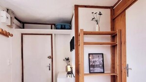 A room with a wooden floor, a white door, a white table with a vase, and a wooden shelf with a picture.
