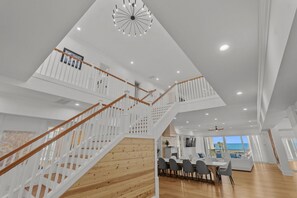 A spacious interior with a wooden staircase, a dining area, and a view of the ocean.