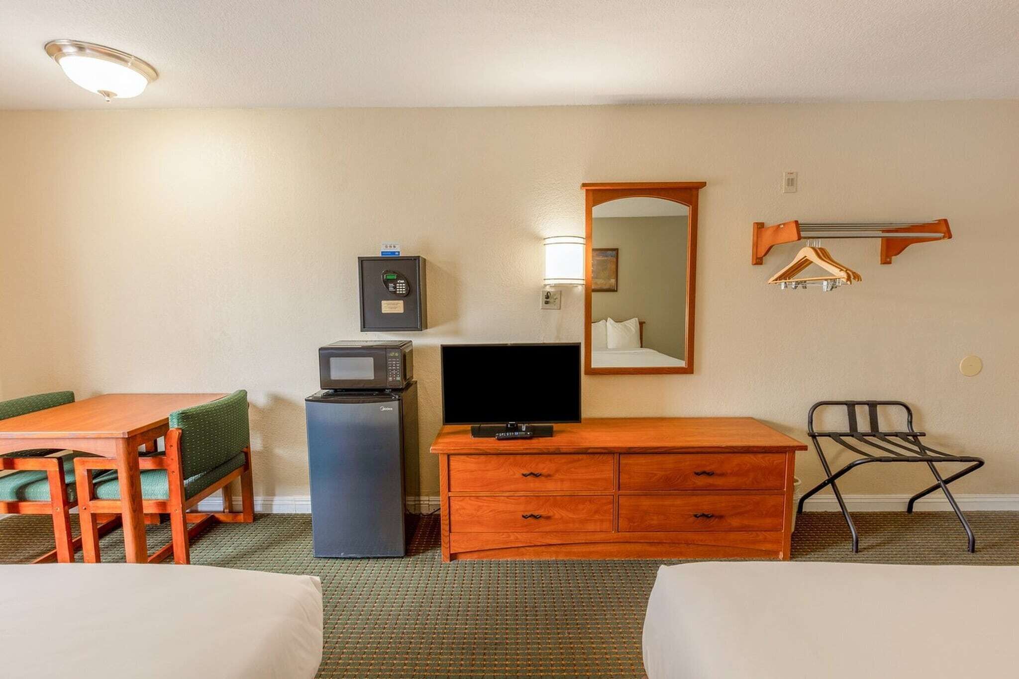 A hotel room with a wooden desk, a television, a microwave, a dresser, a chair, and a bed.