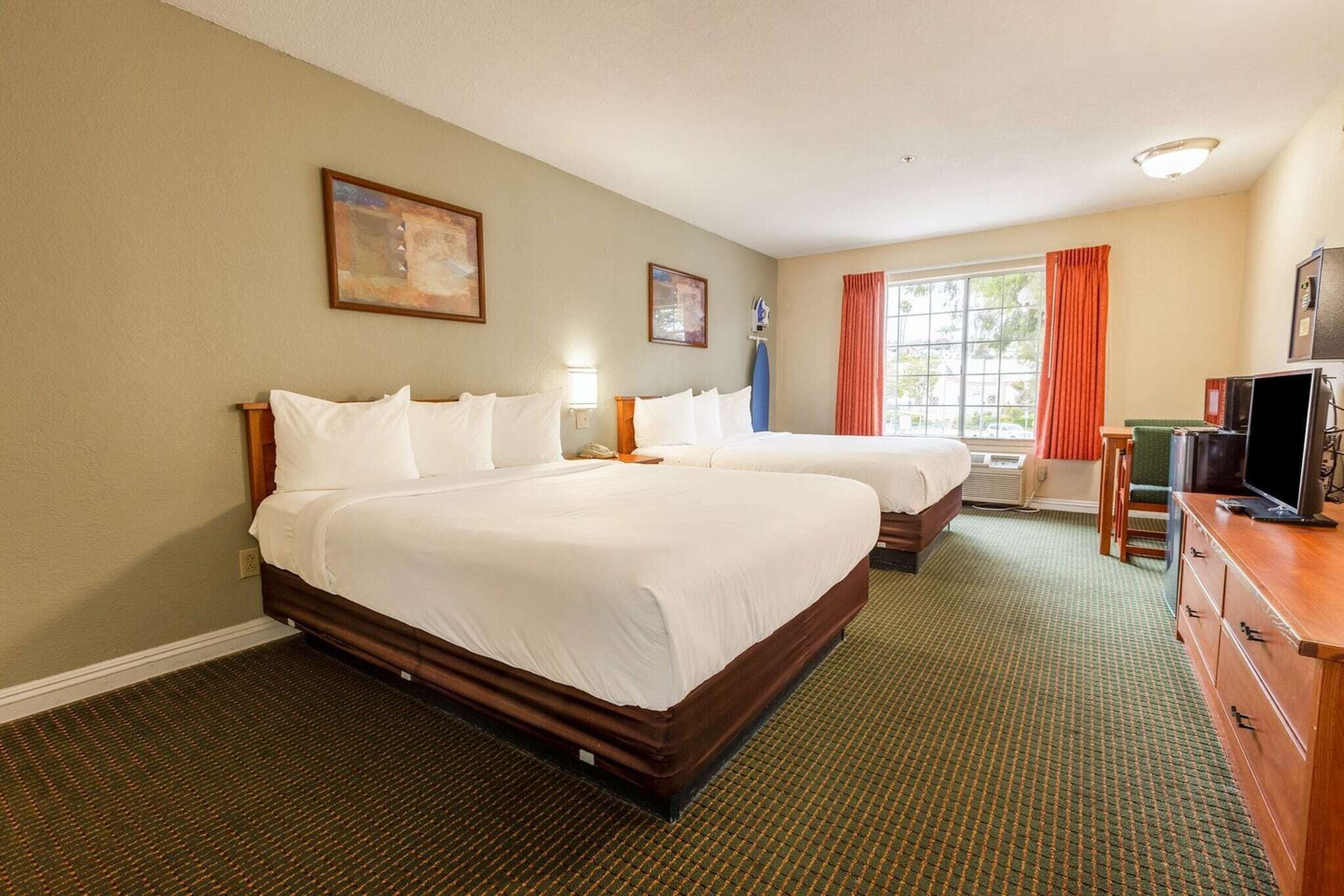 Een hotelkamer met twee bedden, een televisie, een bureau en een raam met gordijnen.