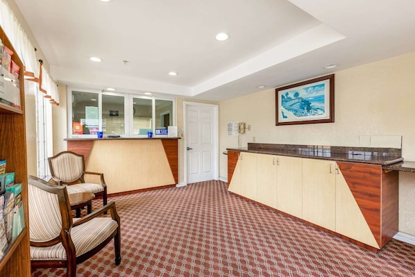 A hotel lobby with a reception desk, a framed picture on the wall, and a patterned carpet.