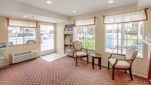 Una habitación de hotel con un ventanal grande, una silla, una mesita y una estantería llena de libros.