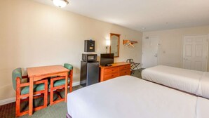 Habitación de hotel con dos camas, un escritorio con silla, cómoda, microondas, televisor y espejo.