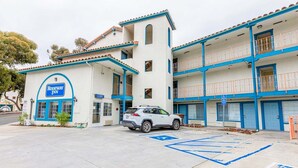 Un motel de dos pisos con una decoración azul y blanca, un estacionamiento y una plaza de aparcamiento accesible para personas con discapacidad.