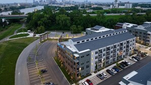 En bygning med flere etager, en parkeringsplads, en flod og en bro i baggrunden.