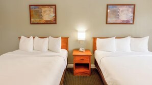 A hotel room with two beds, a nightstand with a lamp, and two abstract paintings on the wall. - 2 Queen Bed | Smoking (San Clemente, CA)