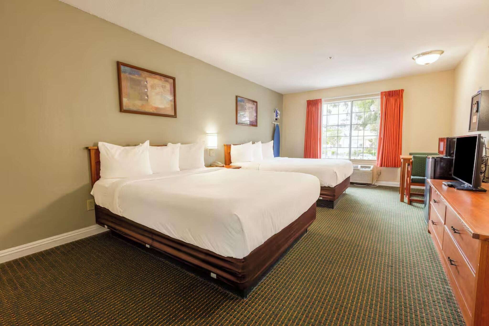 Een hotelkamer met twee bedden, een televisie, een bureau en een raam met gordijnen.