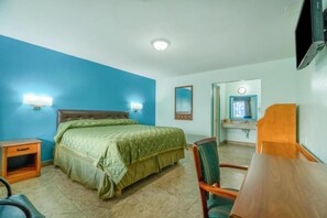 Habitación de hotel con cama, escritorio, silla, televisor, espejo y una mesita.