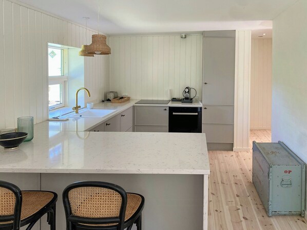 Une cuisine moderne avec des meubles blancs, un îlot central, un lave-vaisselle encastré et un petit réfrigérateur.