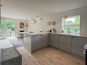 Une cuisine moderne dotée d’un grand îlot central, de planchers en bois et de luminaires suspendus.