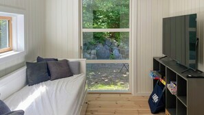 Ett rum med en säng, en tv, en bokhylla och ett fönster med utsikt över grönområden.