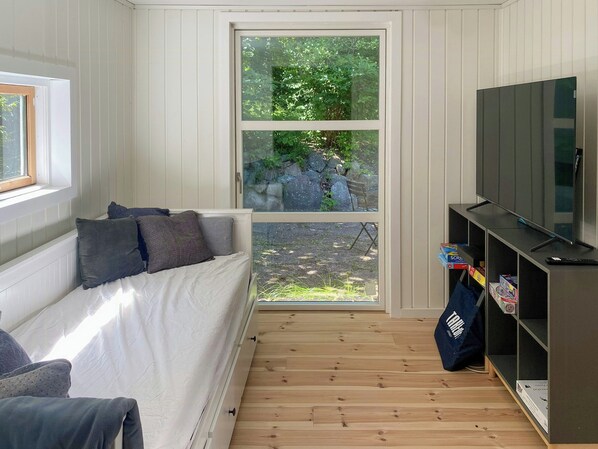 Una habitación con una cama, televisión, estantería y ventana con vistas al verdor.