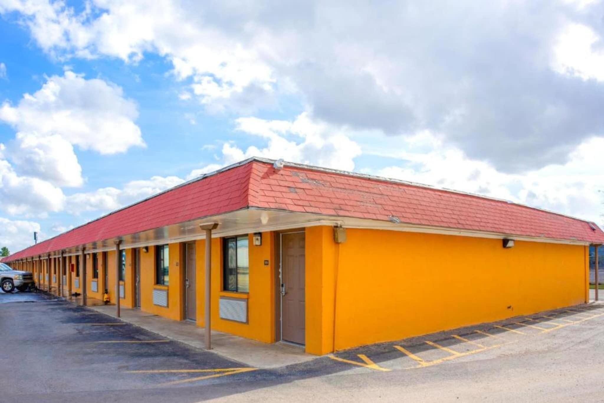 Un motel avec un toit rouge, des murs extérieurs jaunes et un parking.