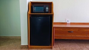 Una kitchenette compacta con microondas y refrigerador, un armario de madera y una pared blanca.