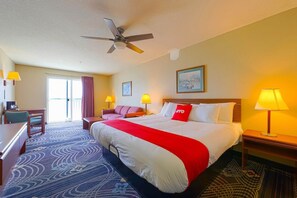 Quarto de hotel com cama, escrivaninha, cadeira e ventoinha no teto.