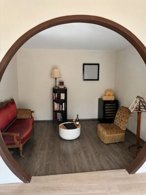A cozy living room with a red sofa, a brown armchair, a bookshelf, and a small round table with a bottle and glass.