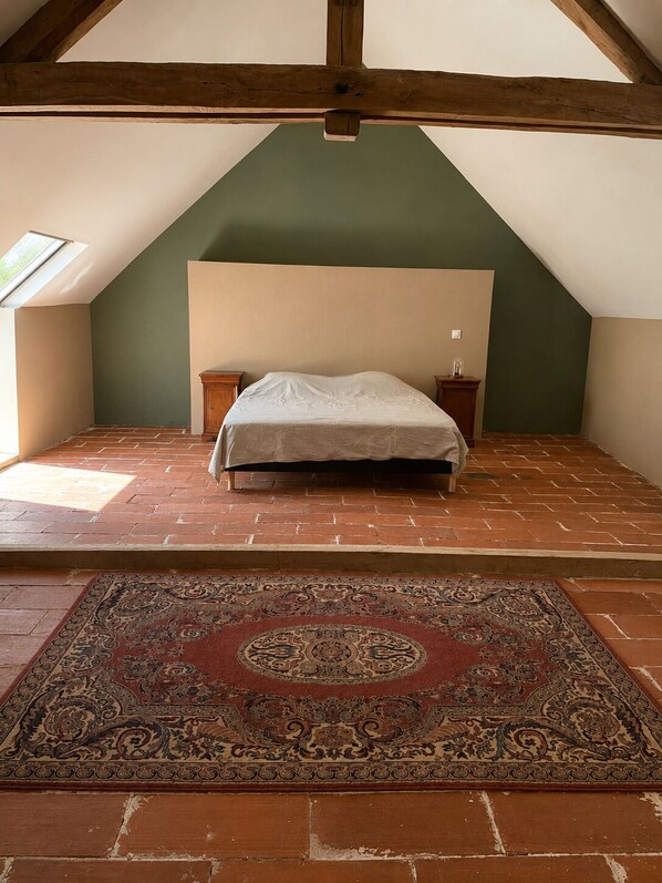 Une pièce avec un plafond en pente, un lit avec une tête de lit, deux tables de chevet, un tapis à motifs et un puits de lumière.